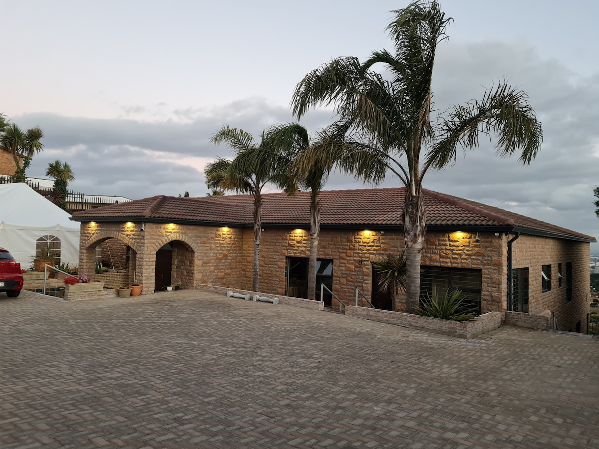 The exterior of the apartment building features a rustic stone facade, accented by palm trees. Warm lights illuminate the structure, enhancing its welcoming appearance. A spacious paved area in the foreground allows for easy access and parking.