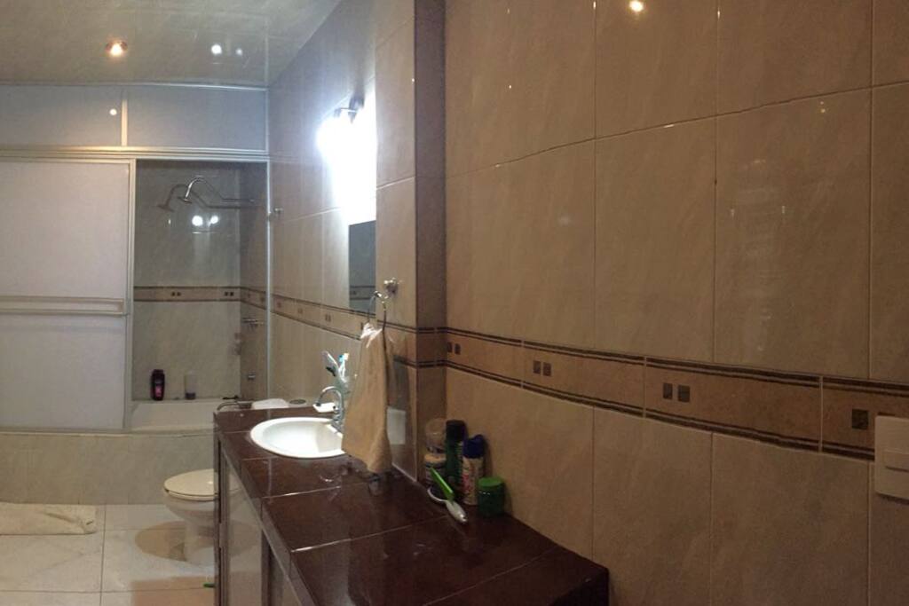 Vista del amplio cuarto de baño con regadera integrada en la tina de baño sencilla, agua caliente.