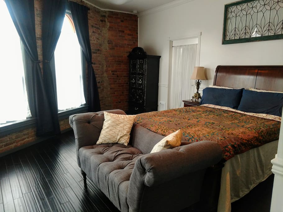 Large Bedroom (350 sq. ft.) with a queen sized bed, settee, four tall windows, heating/air conditioning, ceiling fan, and closet space.