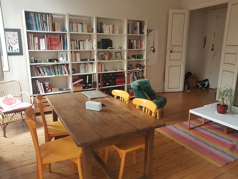 Grand salon lumineux, avec parquet au sol, comme dans tout l'appartement, table pour 6 personnes et canapé lit.