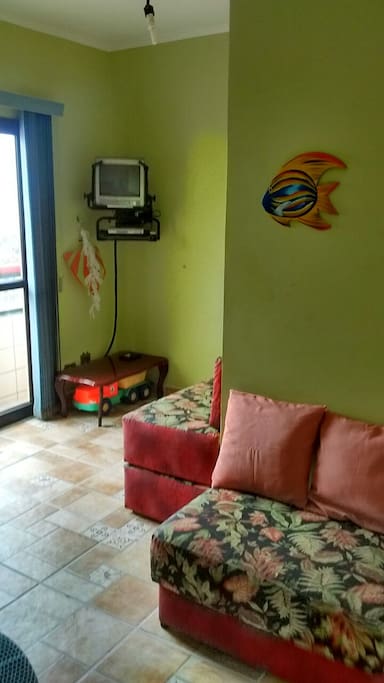 Sala em L, com sofá cama, tv, brinquedo de praia.