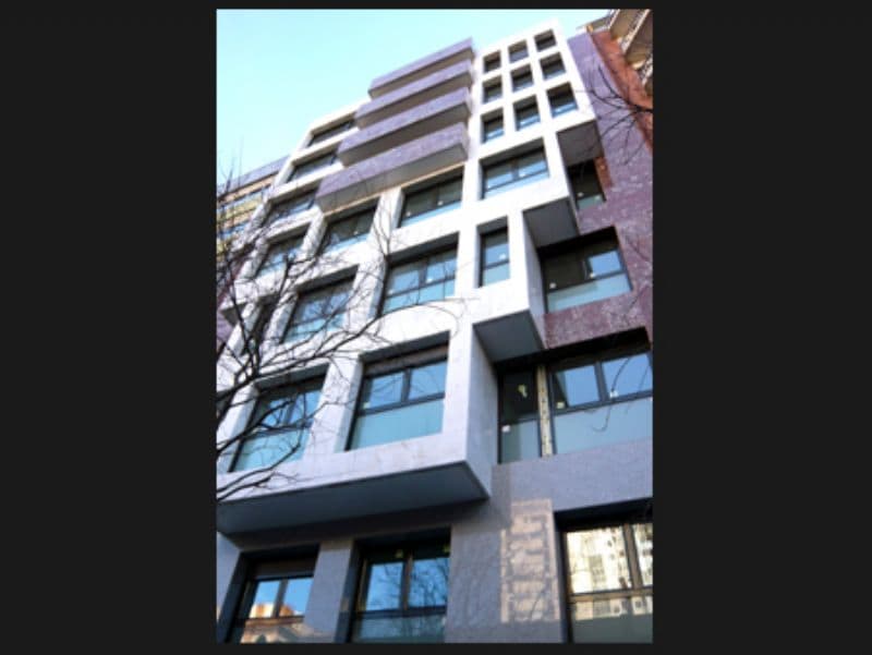 A modern apartment building features a mix of textured facades, with large windows that provide ample natural light. The architecture combines geometric shapes in a contemporary style, and the exterior is accented by a muted color palette.