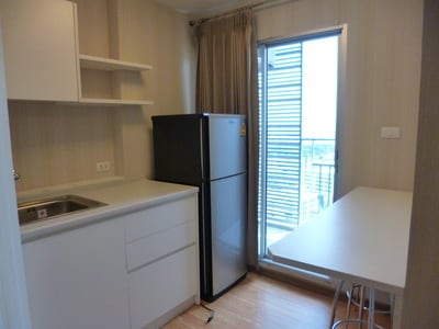 A well-equipped kitchen area is featured, showcasing a refrigerator, a sink with cabinetry, and a dining table positioned beside a window. Natural light enters through the sliding glass door, which provides access to a balcony, enhancing the spacious feel of the room.