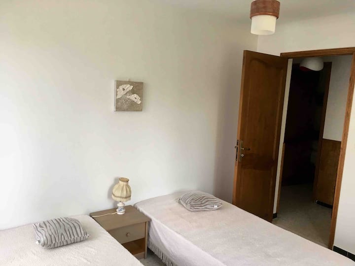 Dormitorio 4 con vistas a la terraza exterior, compuesto por dos camas de 90, una mesita de noche y un armario de pared.