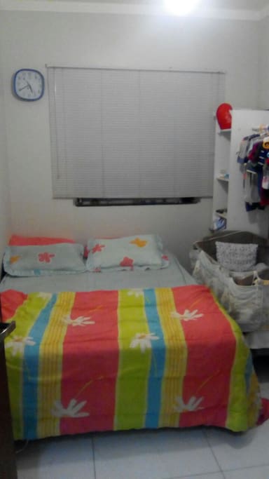 Quarto com cama de casal ortopédica, espaço para colchão no chão, guarda roupa, prateleiras e arara para o hóspede guardar seus pertences, ventilador de teto, janela com persiana contra o sol. Roupa de cama disponível. Obs este berço da foto e demais pertences não estão no quarto.