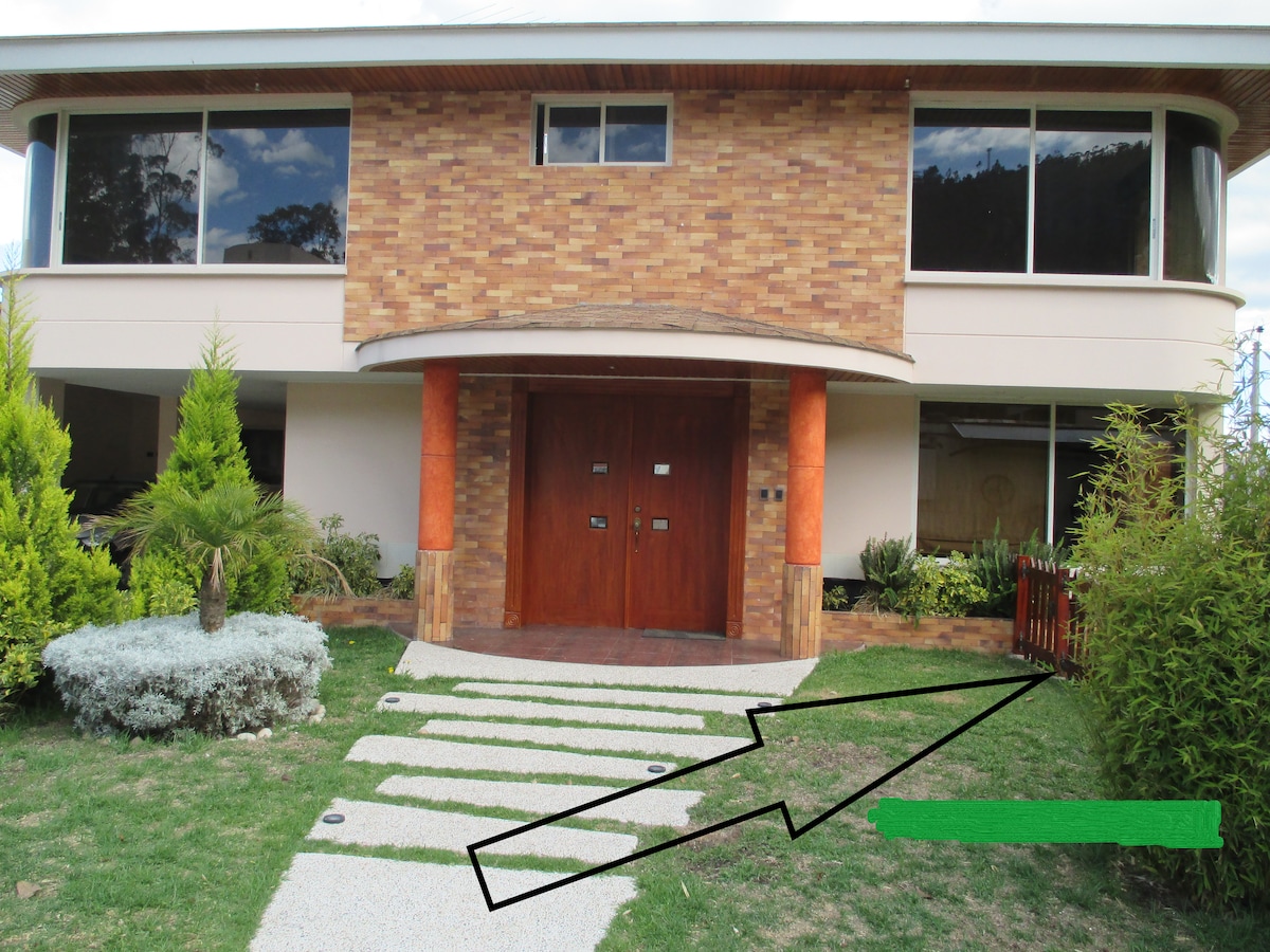 The exterior view of the property features a two-story brick facade with large windows. A well-manicured lawn is visible, flanked by neatly trimmed shrubs and trees. A stone path leads to a double wooden door, inviting guests to enter the welcoming space.