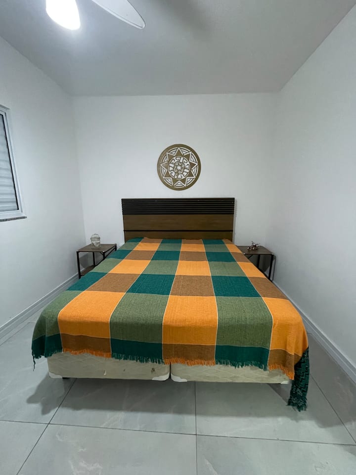 Schlafzimmer mit Boxspringbett, Zimmermädchen, offenem Kleiderschrank, Spiegel und Deckenventilator.