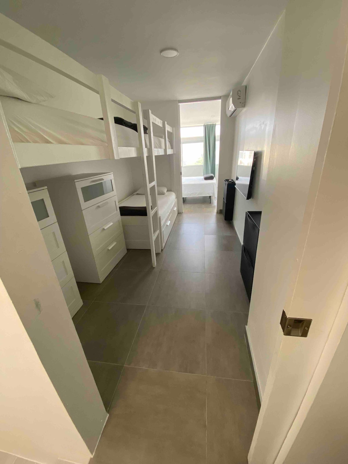 3 eenpersoonsbedden georganiseerd in stapelbedformaat met tv en 2 dressoirs en schoenenopslag 