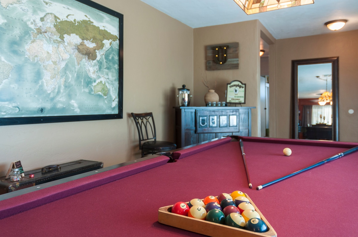 A game room designed for leisure features a classic billiard table adorned with rich burgundy felt. A vibrant world map is displayed on the wall, adding an element of exploration. Nearby, a dark wooden cabinet holds various games and entertainment accessories.