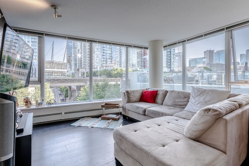 floor to ceiling wide windows from living room with comfortable clean sectional couch and 60" flat screen TV