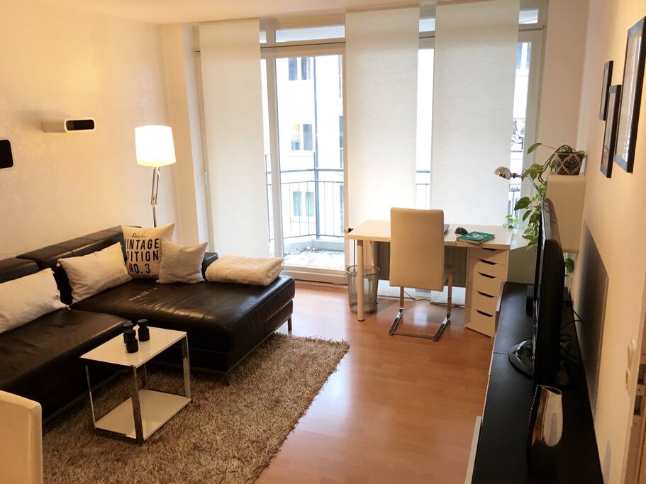 Große Dreisitzer-Couch, kleiner integrierter Arbeitsplatz und Balkon zur ruhigen Seitenstraße. / Large sofa, integrated workplace and balcony to a quiet residential street.