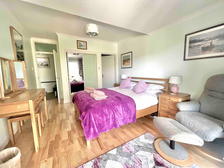 غرفة نوم رئيسية مبهجة ومتجددة الهواء مع حمام داخلي وتلفزيون ذكي مثبت على الحائط. أبواب منزلقة مباشرة إلى منطقة الجلوس الخارجية. 