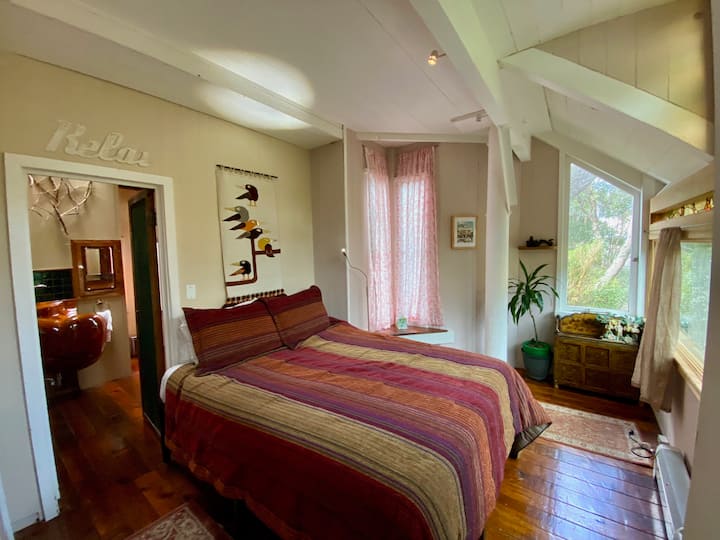 Spálňa na 2. poschodí s manželskou posteľou veľkosti Queen.  Pripojená kúpeľňa je viditeľná. 