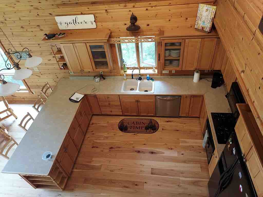 An overhead view of the kitchen reveals wooden cabinetry and a spacious countertop. Double sinks are positioned beneath a window, providing natural light. An island with bar seating is visible, alongside modern appliances, creating a warm and functional cooking area.