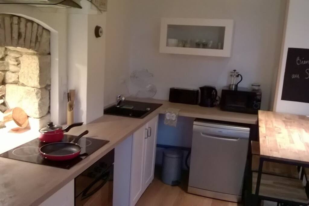 Cuisine toute équipée, ancienne cheminée face aux plaques de cuisson, table haute et tabourets