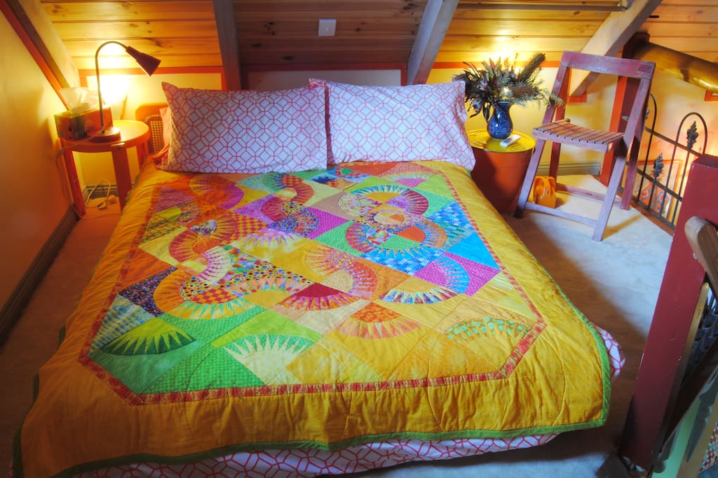 A beautiful, vibrant handmade quilt and fine linen on a double bed in the loft. The bed is on a low wooden frame but comfortable and with room to stand under the high rafters and a spacious feel .
