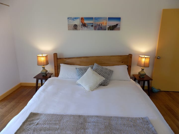 سرير بحجم كبير مع لوحة رأس خشبية مصنوعة يدويًا من خشب المانجو في غرفة النوم الرئيسية.