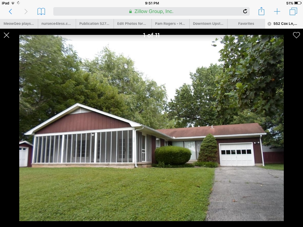 The exterior of the house is shown, featuring a large screened front porch that invites fresh air. The facade is complemented by a well-maintained lawn and a small bush. A driveway leads to a one-car garage, with tall trees providing shade in the background.