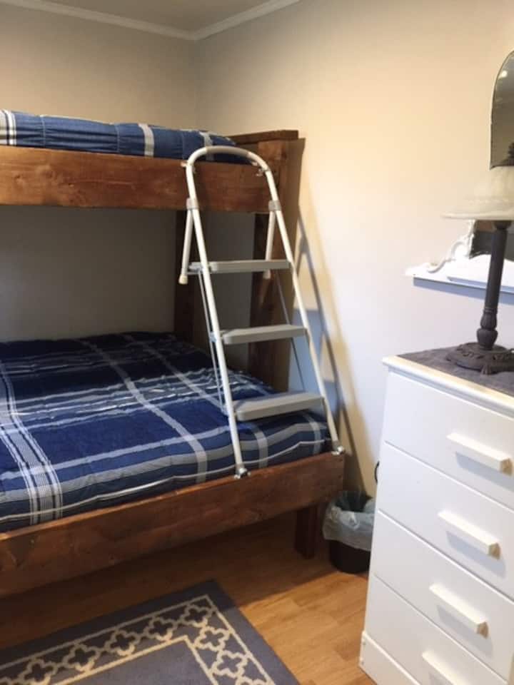 The Main bedroom has a single bed on top and a queen on the lower. A dresser provides extra storage. There is an ironing board and iron behind the door.