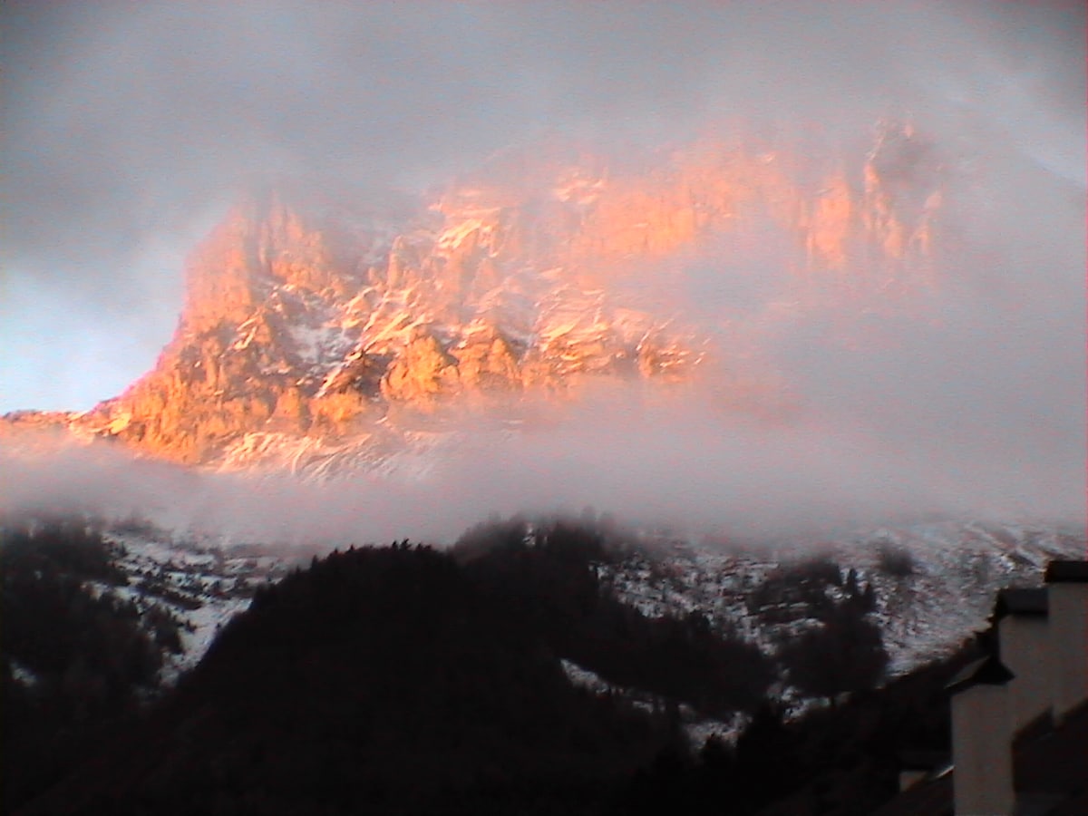 The Grand Veymont mountain peak is outlined by soft morning light, revealing its rugged contours. Fluffy clouds partially obscure the summit, while lower slopes show hints of snow and greenery, creating a serene and tranquil backdrop in the early hours.