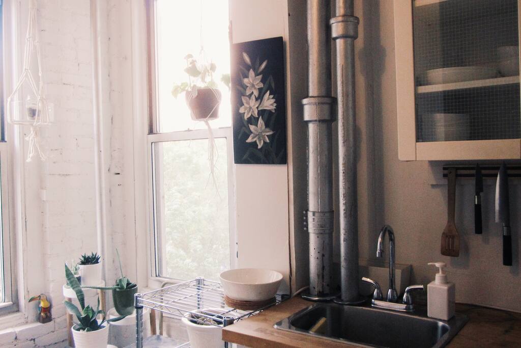 Bright kitchen with plants and a small stool to sit and enjoy coffee or tea at the window. Not pictured is full size fridge and gas range/oven.