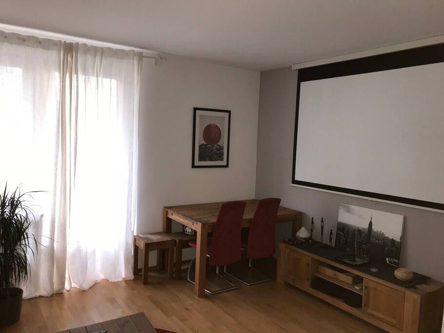 Living room is equipped with dining table and beamer and provides access to balcony