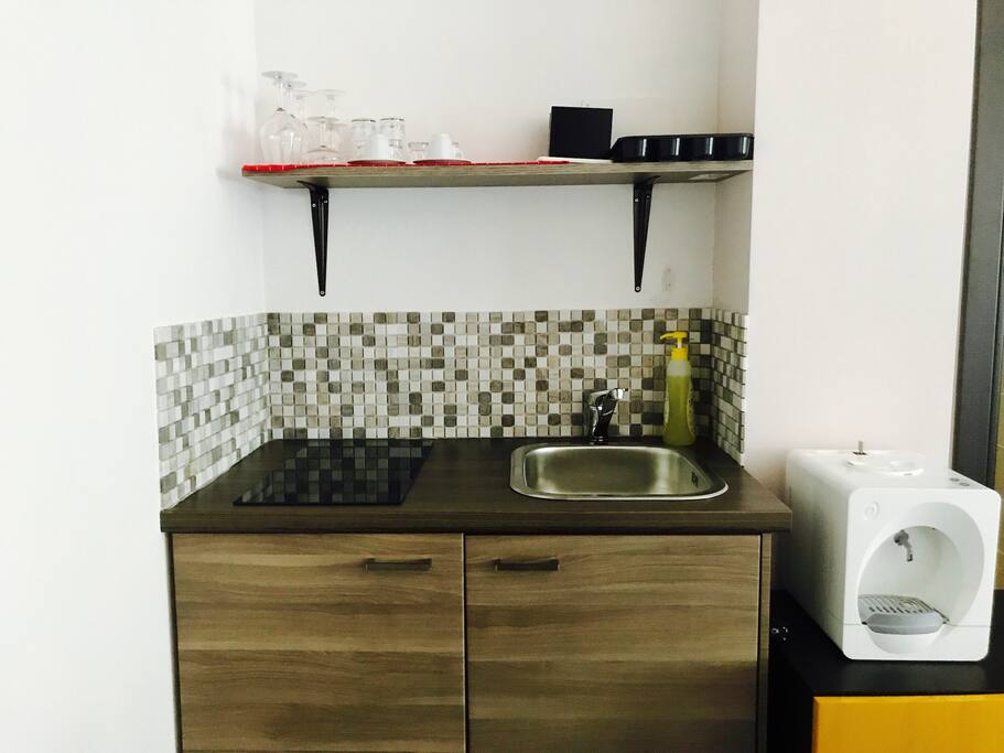 Angolo cottura con pianale ad induzione, lavello, utensili base da cucina e macchina del caffè.