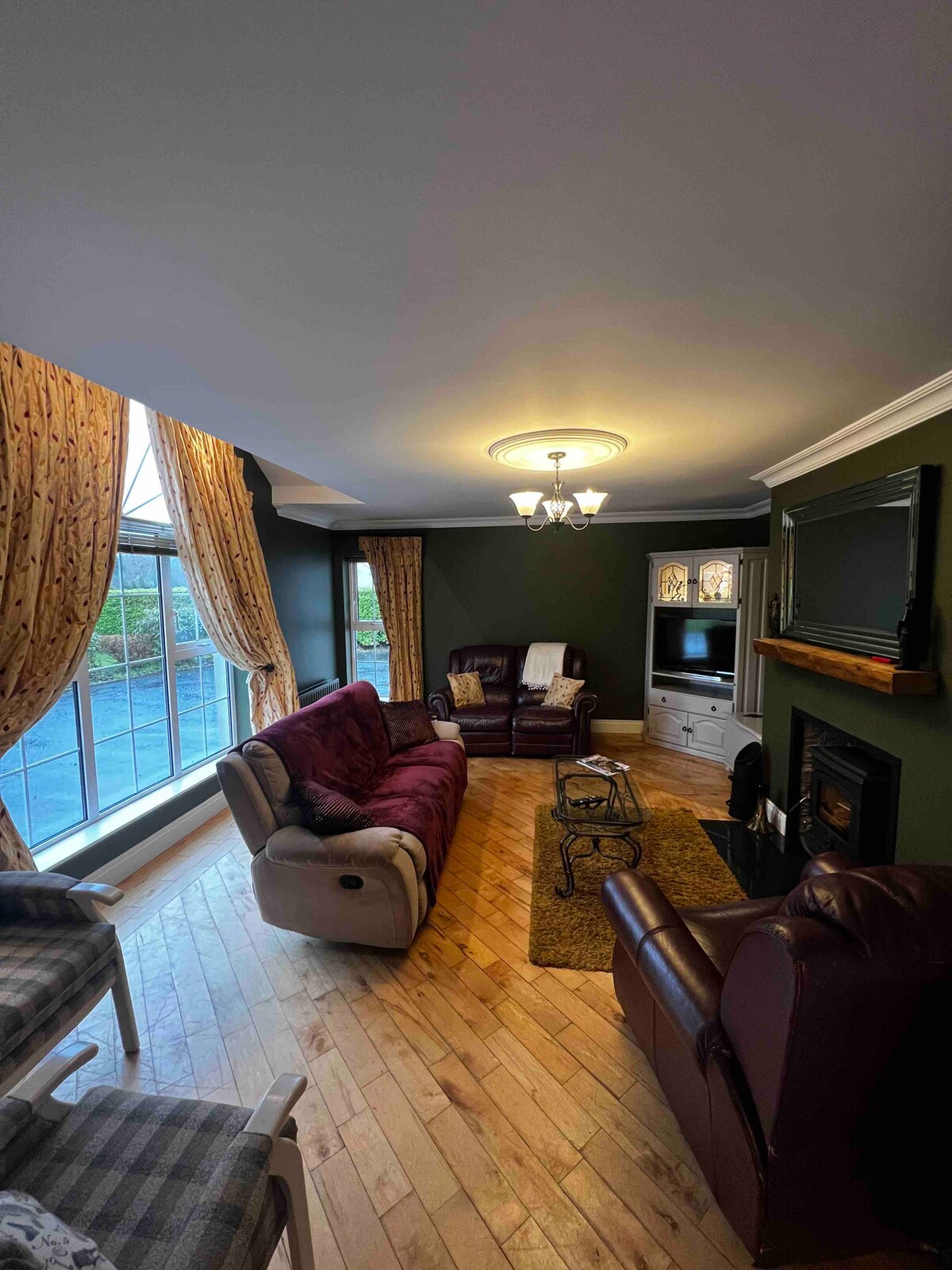 A welcoming living area is featured with comfortable seating, including plush sofas and armchairs. Large windows allow natural light to fill the space, complemented by soft drapery. A television is positioned on the wall, and a fireplace adds warmth to the atmosphere.