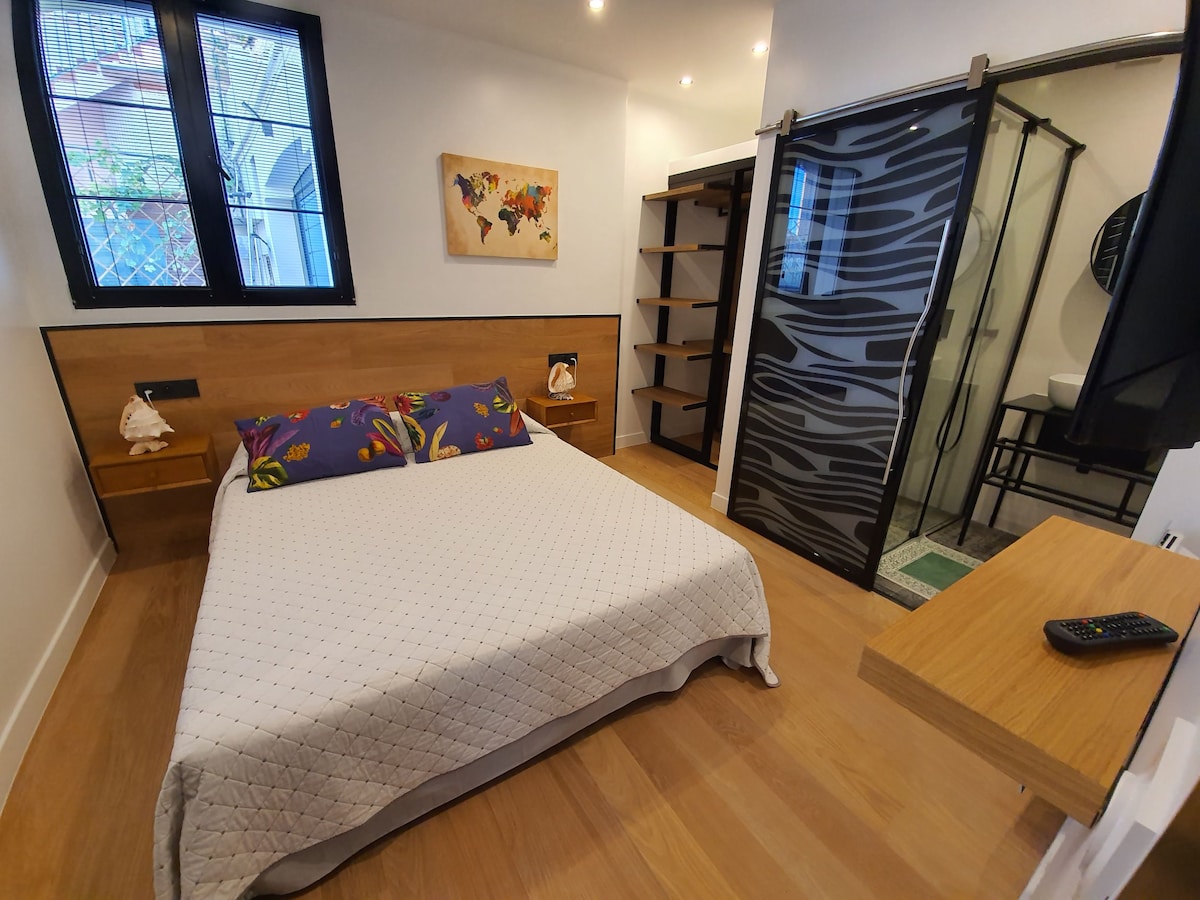 Dormitorio con zona de ducha con cama doble y lavabo.