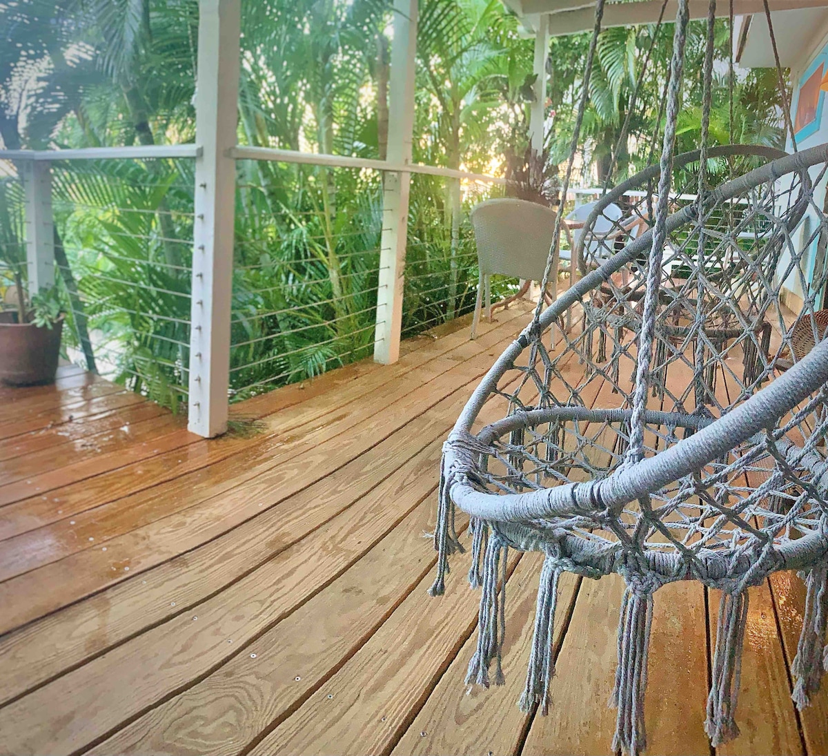 A comfortable hanging chair is positioned on a wooden deck, surrounded by lush green foliage. Natural light filters through the plants, creating a serene atmosphere. The spacious area invites relaxation with its warm tones and smooth finish, enhancing the connection to the outdoors.