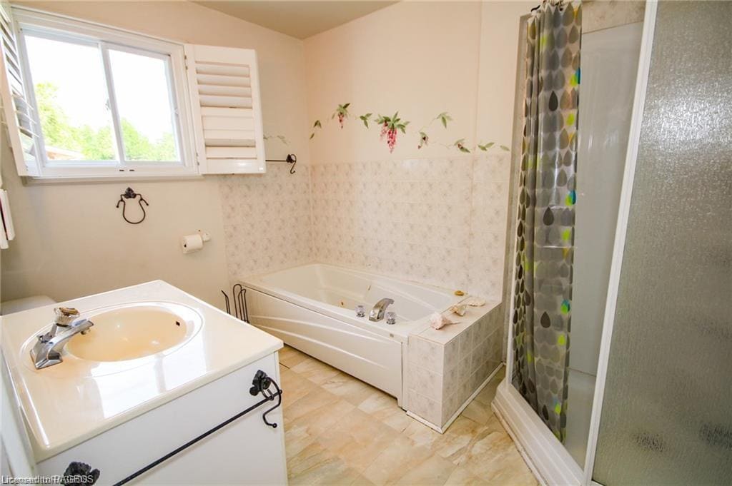 A bright bathroom features a soaker tub with a flower accent above and a separate glass shower. A light-colored vanity with a sink is positioned beside the tub, while a window allows natural light to illuminate the space.