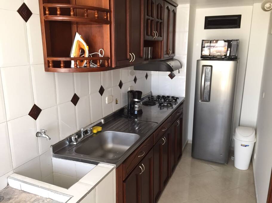 Cocina con nevera, horno microondas, cafetera, vajilla y cubiertos para 4 puestos.