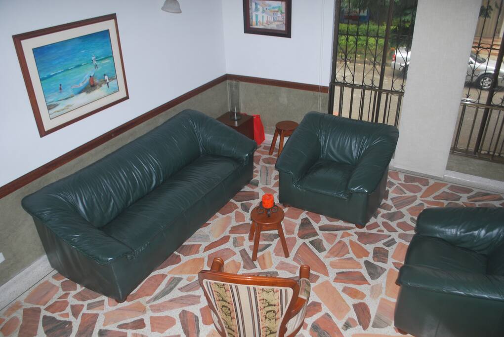 Sala con muebles de cuero, piso de marmol y techo alto.