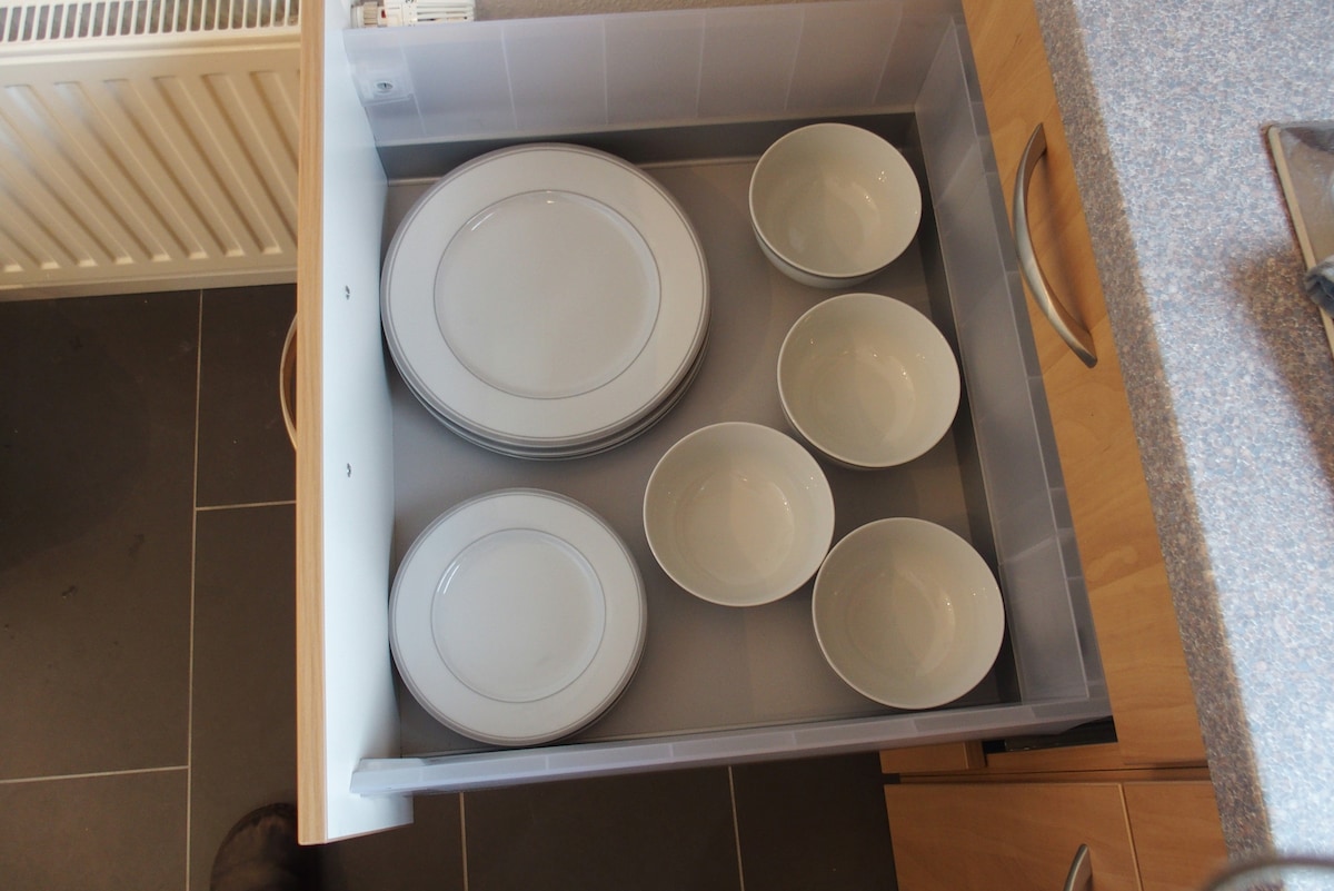 A kitchen drawer is shown containing a set of white plates and bowls. The plates are stacked neatly, while the bowls are arranged next to them, providing an organized storage space for dining essentials.
