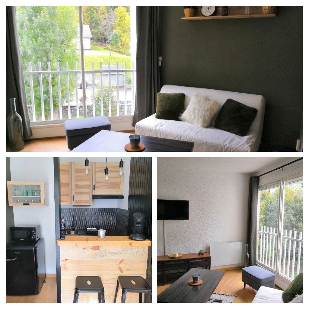 A cozy living area features a neutral-toned sofa with decorative pillows and a small coffee table. A kitchenette with wood accents is visible, equipped with a coffee maker and mini-fridge. Large windows allow natural light to enter, with views of greenery outside.