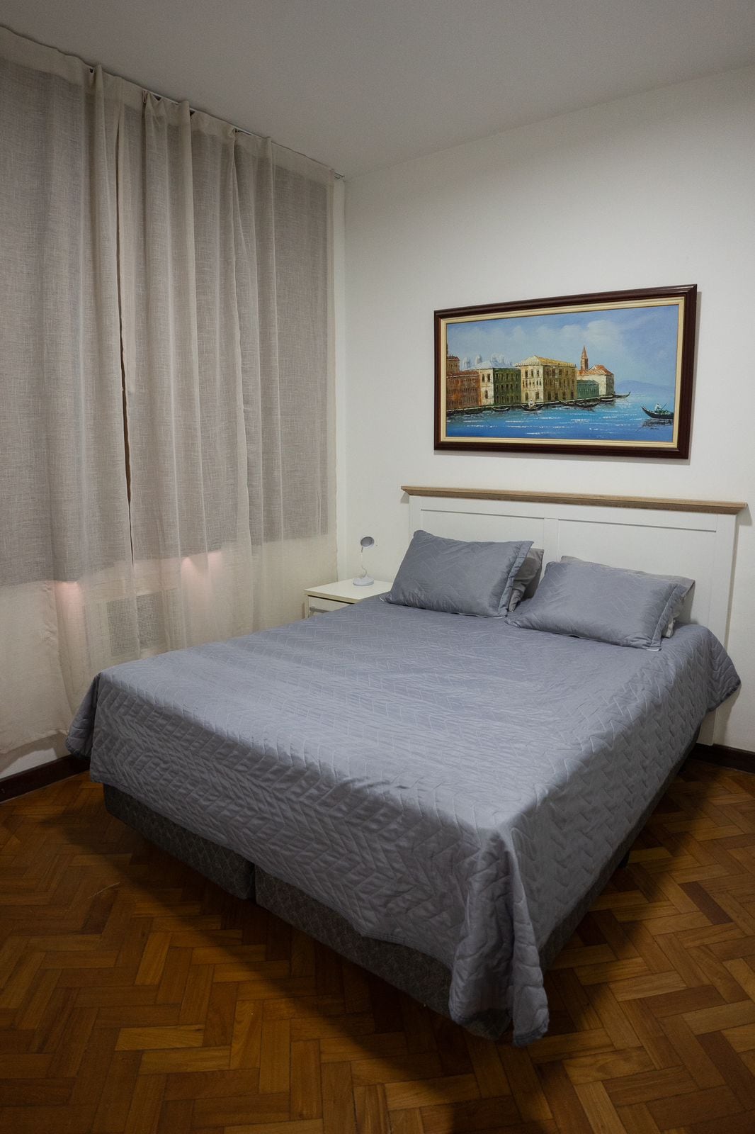 غرفة أصغر وسرير بحجم كوين ومرآة وكرسي واحد وطاولة بجانب السرير ومصباح ومكيف هواء