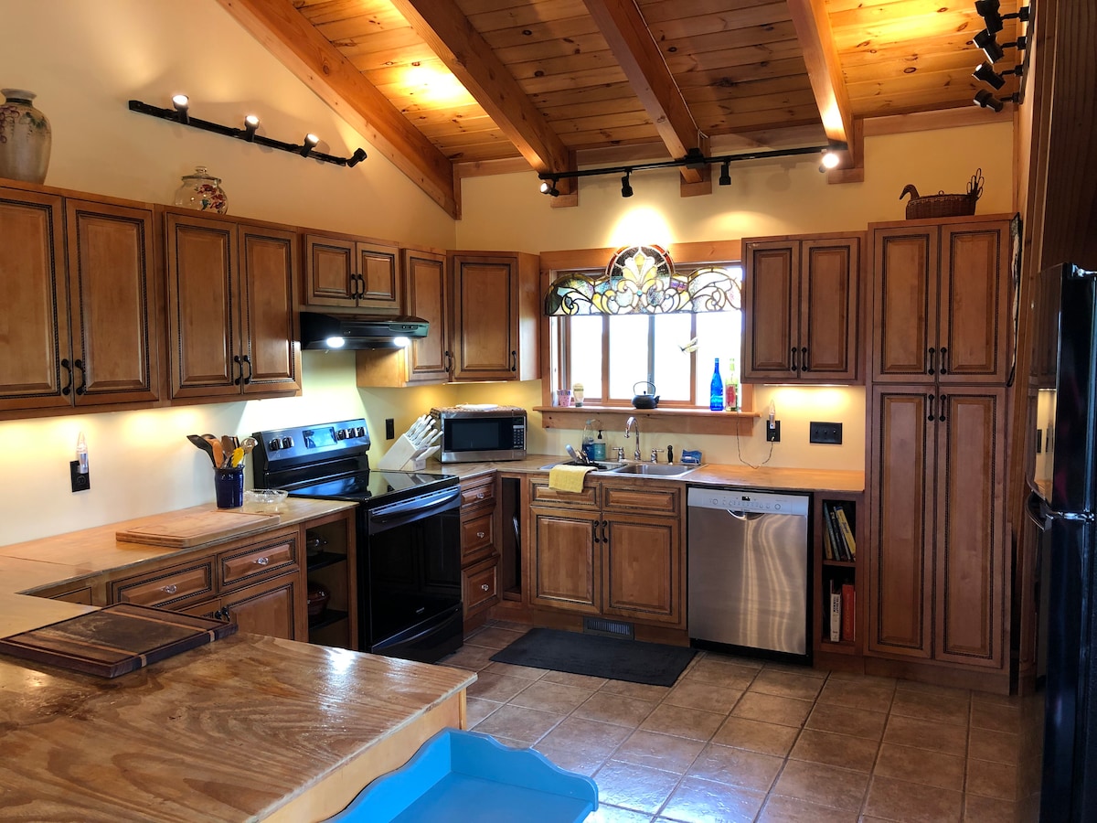A spacious kitchen is highlighted by wooden cabinetry and natural light from a window adorned with stained glass. Modern appliances, including an oven and dishwasher, are seamlessly integrated. The tiled flooring complements the warm wood accents, creating a functional cooking space.