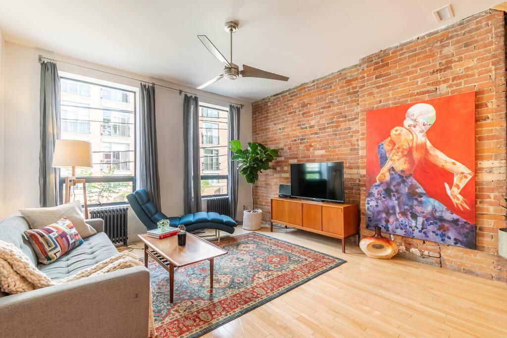 Spacious living room with exposed brick wall, mid-century modern furniture and floor to ceiling windows overlooking Queen West