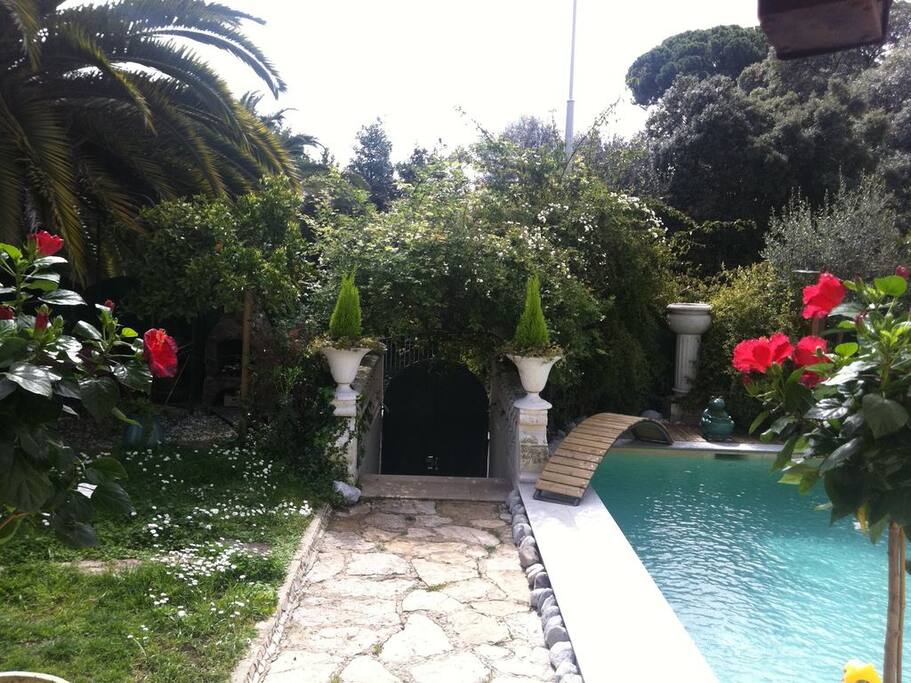 Vue de la porte d'entrée de la villa : la partie sud du jardin, piscine à droite, salon de jardin avec barbecue à gauche.