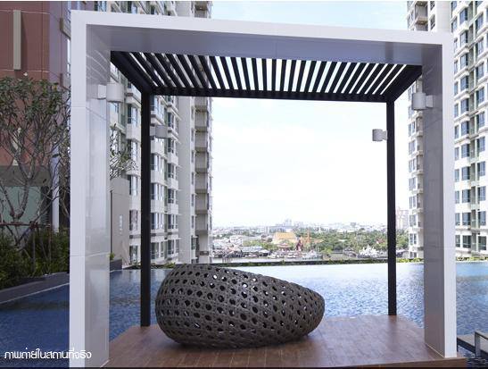 A modern shaded gazebo frames a unique oval-shaped seating area crafted from intricately woven material. The backdrop displays views of the swimming pool and surrounding urban landscape, contributing to a serene atmosphere for relaxation.