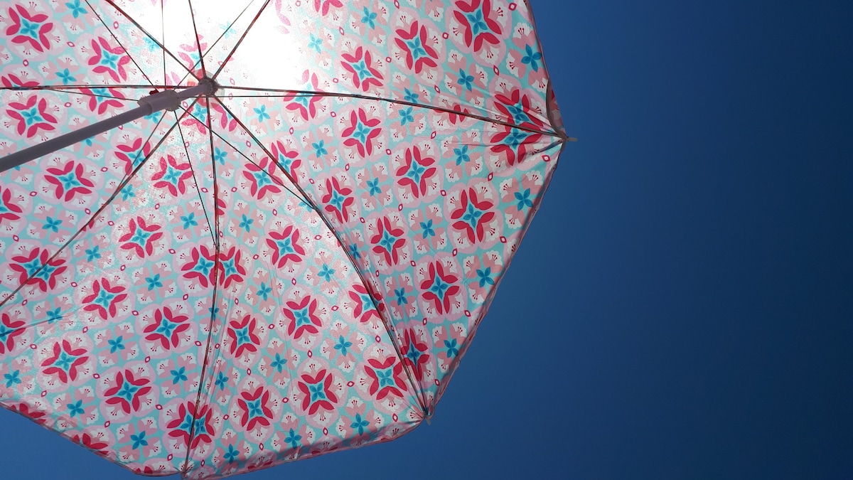 A colorful beach umbrella is positioned against a clear blue sky. The umbrella features a vibrant floral pattern, with shades of pink and turquoise, providing shade and a cheerful touch for outdoor relaxation.