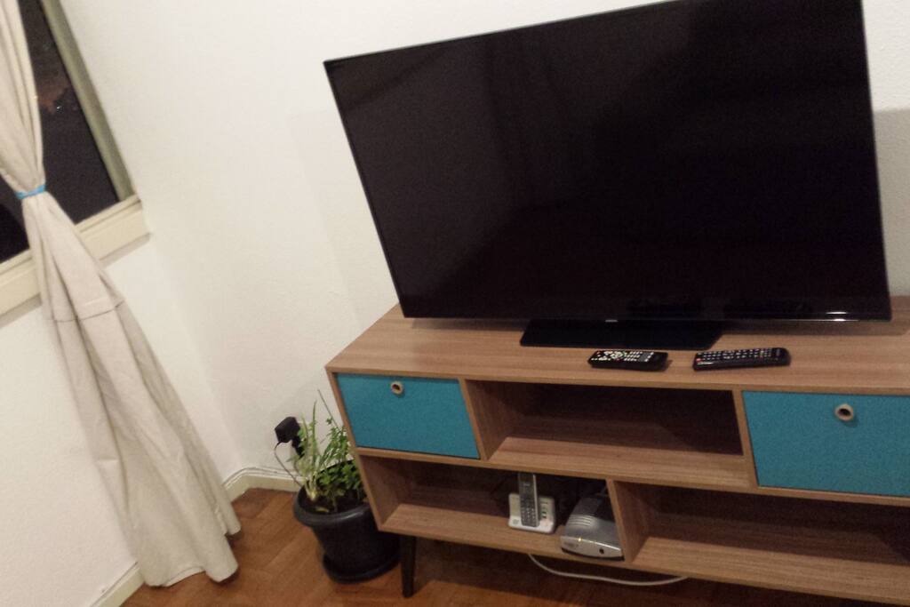 Televisão grande na sala, rack, TV a cabo e internet wi-fi.