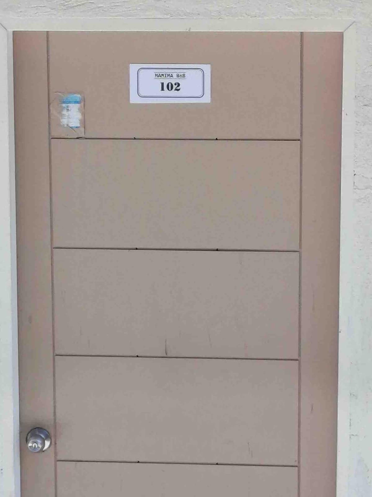A simple door is displayed, featuring a beige color with horizontal lines. A numbered sign reads 'Room 102' at the top, and a round door knob is situated on the right side.