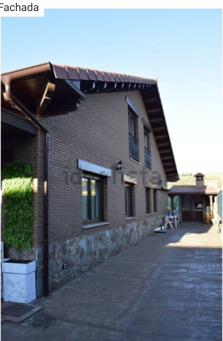 The exterior facade showcases a two-story building with a combination of brick and stone materials. Large windows create an inviting look, and a covered outdoor space is visible on the right, providing additional leisure opportunities.