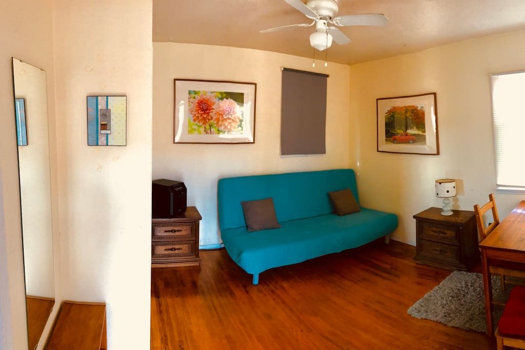 MAIN ROOM: Comfortable futon in sofa mode, window shade closed. Hardwood floor, table for desk or dining.