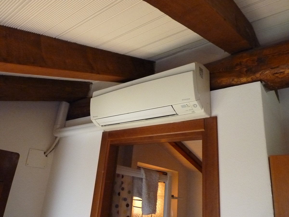 An air conditioning unit is mounted on the wall near the wooden beams, providing comfort to the living space. The unit is positioned above a doorway, seamlessly blending with the interior design.