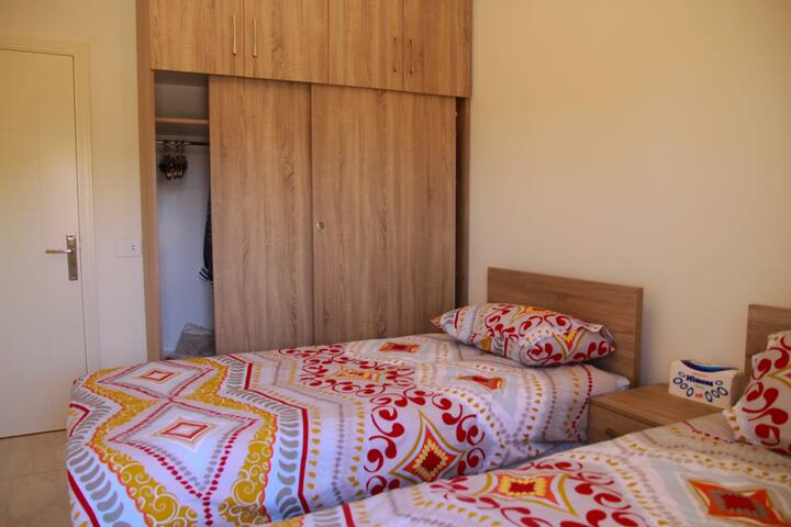 Chumba cha kulala chenye vitanda viwili ikiwemo ukuta kwenye kabati ambalo lina viango na kabati la kuweka vitu 