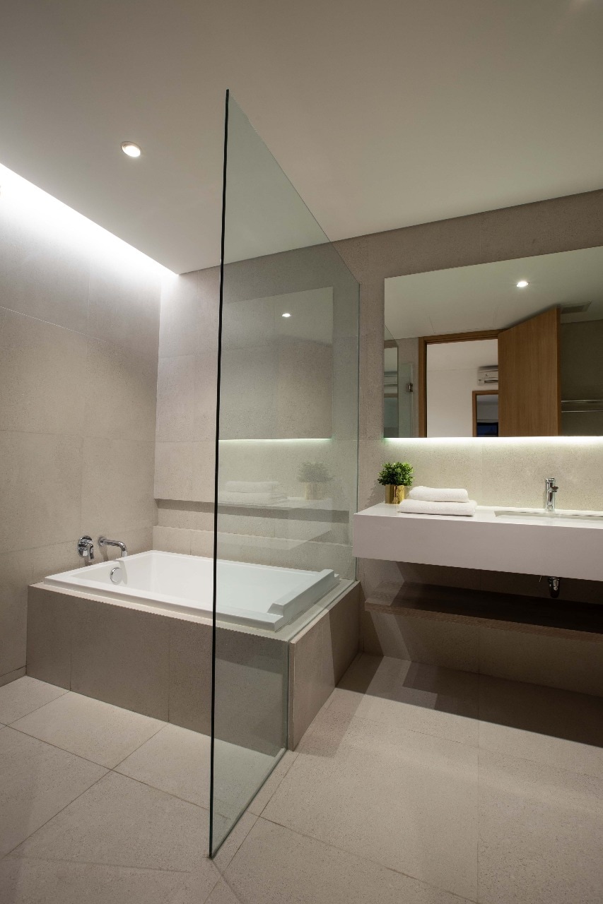 A modern bathroom is depicted, featuring a sleek glass-enclosed shower alongside a spacious bathtub. A minimalist vanity with a white countertop is shown, complemented by neatly arranged towels. Soft ambient lighting enhances the contemporary design, creating a clean and serene atmosphere.