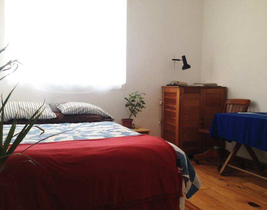 Bedroom with queen size bed, one little table with a chair and a little drawer.