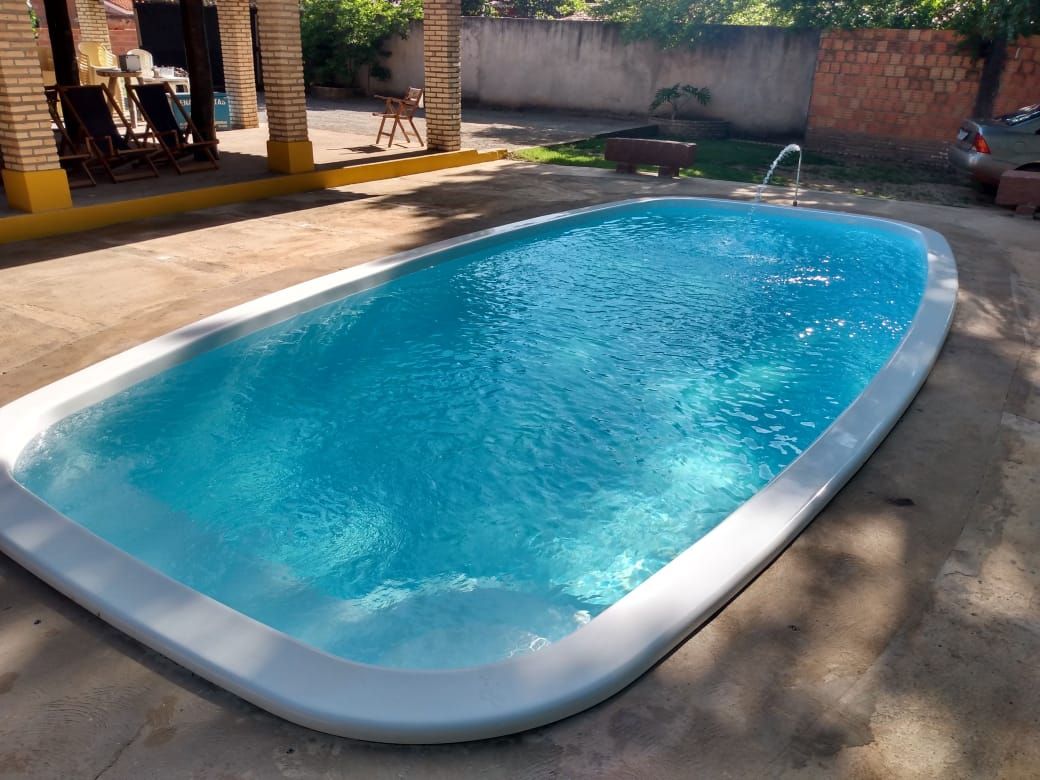 A clear, inviting swimming pool is set within a spacious outdoor area. Sunlight reflects on the water's surface, highlighting the pool's smooth, rounded edges. Surrounding greenery and shaded spaces contribute to a relaxing atmosphere.